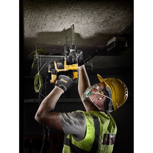 Worker wearing safety gear uses a DEWALT drill to make a hole in a ceiling at a construction site.