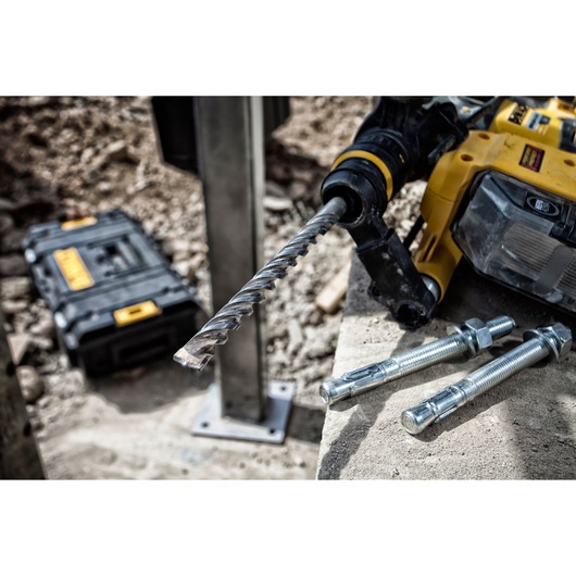 DEWALT drill with masonry bit and bolts on concrete, tool case in background at construction site.
