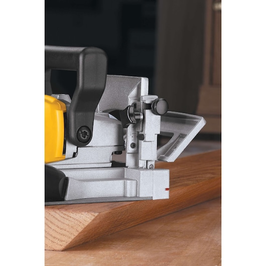 Close-up view of a DEWALT biscuit joiner DW682K being used on a wooden board. The tool's metal and plastic parts, adjustment knobs, and guide are clearly visible.