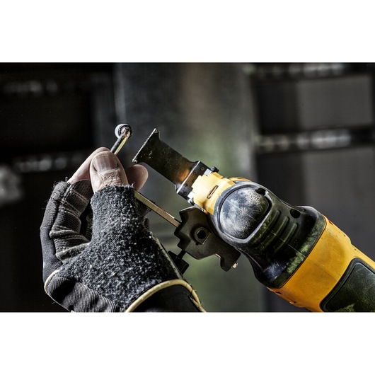 A hand wearing a work glove is holding a metal object near the blade of a yellow and black DEWALT oscillating multi-tool.