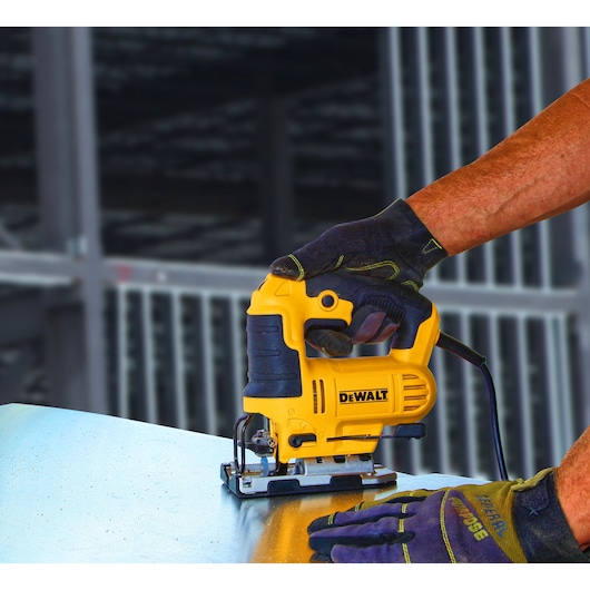 A person wearing gloves is using a yellow and black DEWALT jigsaw to cut a metal sheet.
