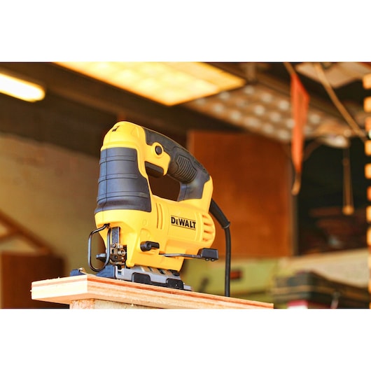 A yellow and black DEWALT electric jigsaw is shown placed upright on a piece of wood in a workshop setting.