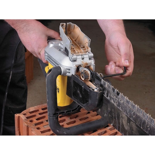 A person is using a hex key to adjust or maintain a DEWALT electric masonry saw, which has its cover open and is placed on top of a brick.