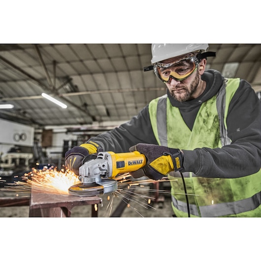 Worker using DEWALT DWE4036 angle grinder, producing sparks on metal in an industrial workshop.