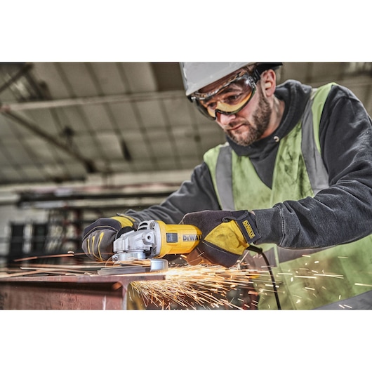 Worker grinds metal with DEWALT DWE4036 angle grinder, creating sparks in an industrial workshop.