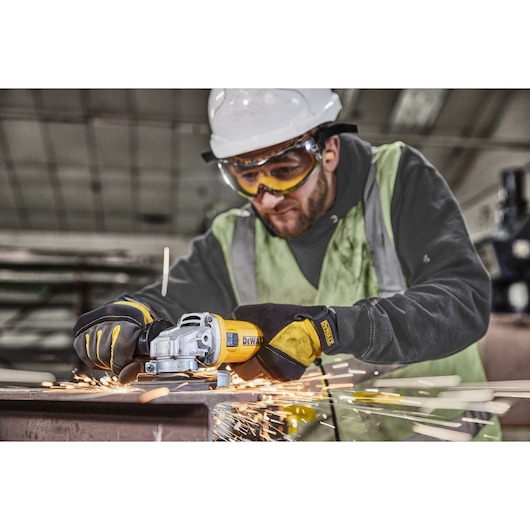 Worker uses DEWALT DWE4036 angle grinder on metal, gloves and sparks visible in industrial setting.