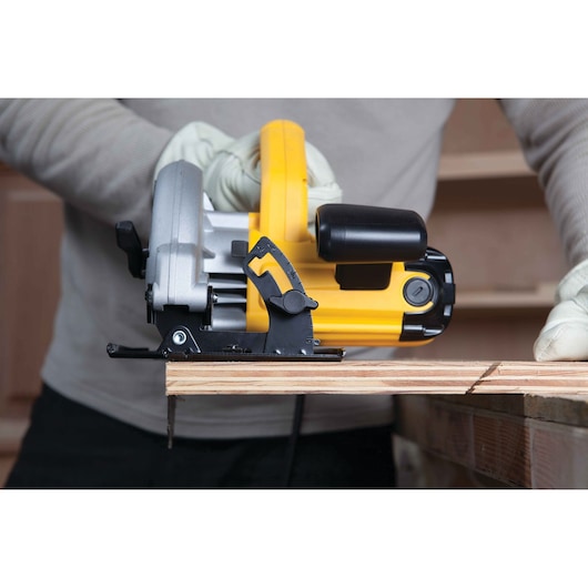 A person wearing gloves is using a yellow and black DEWALT circular saw to cut a piece of wood.
