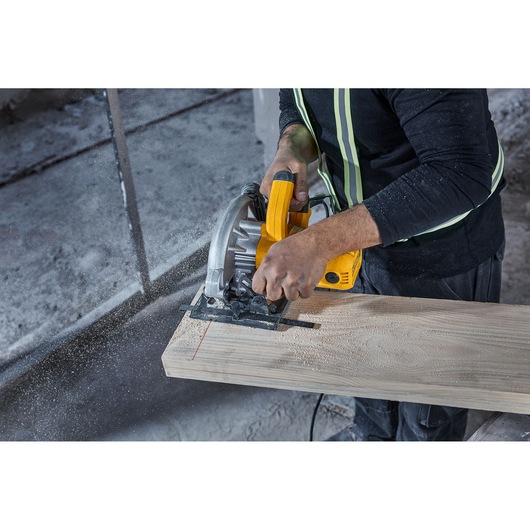 A person using a yellow DEWALT circular saw (model DWE5615) to cut a wooden plank, with sawdust and safety gear visible.