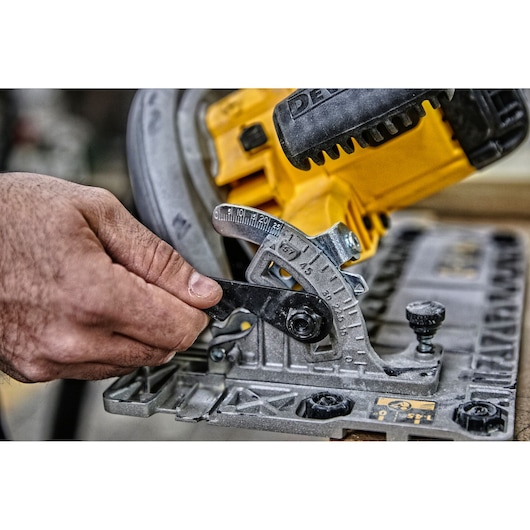 Close-up of a hand adjusting the angle gauge on a yellow DEWALT circular saw.