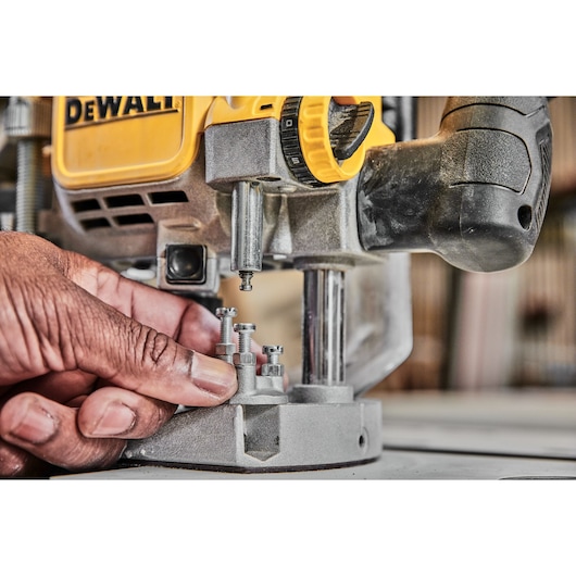 Close-up of a hand adjusting bolts on a DEWALT power tool, likely a router, with a yellow and black body.