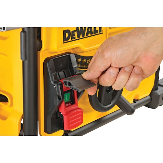 Close-up of a hand operating the power switch on a yellow DEWALT table saw, with focus on the safety cover being lifted.