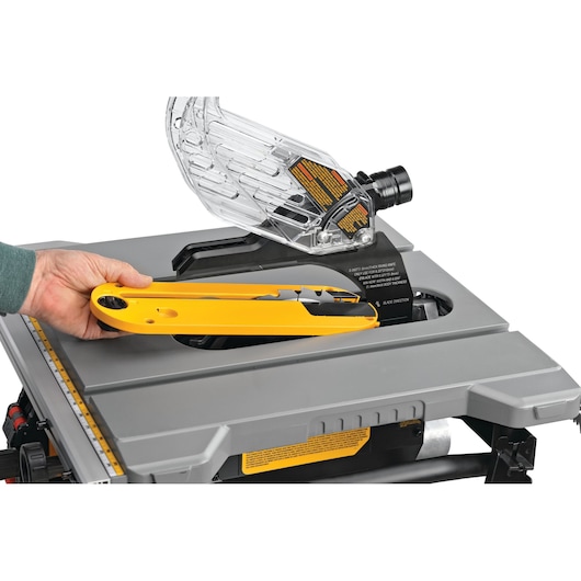 Close-up of a person placing a yellow insert into the slot of a DEWALT table saw, with a transparent blade guard attached.
