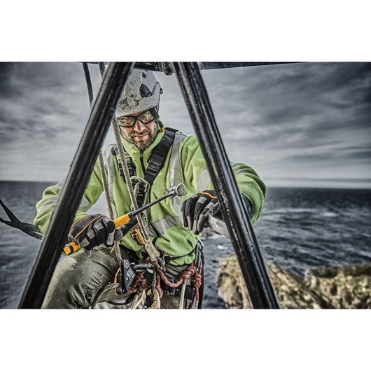 Worker with safety harness using a DEWALT tool on a structure outdoors near the sea.