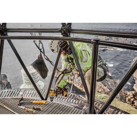 Worker using DEWALT tools inside a lighthouse with a sea view, wearing safety gear and helmet.