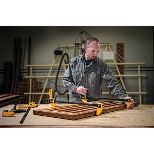 Person uses DEWALT clamps to secure wooden boards on a workbench in a workshop.