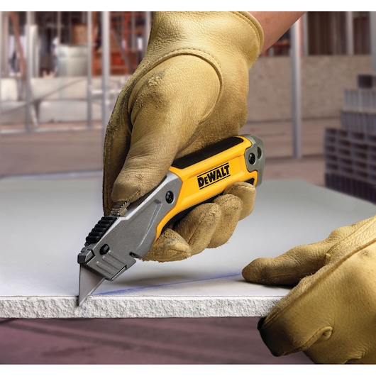 Gloved hand cutting material with a DEWALT utility knife at a construction site.