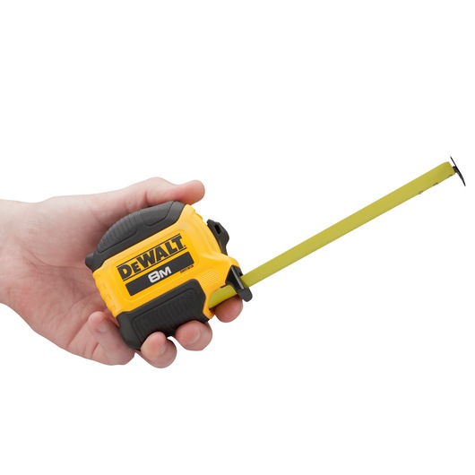 Hand holding a yellow DEWALT 8M tape measure with the tape extended.