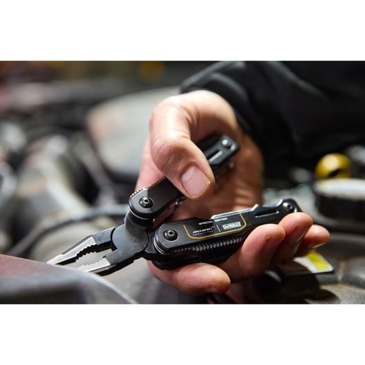 Hand holding a DEWALT black multi-tool with pliers, used for mechanical work in a workshop setting.