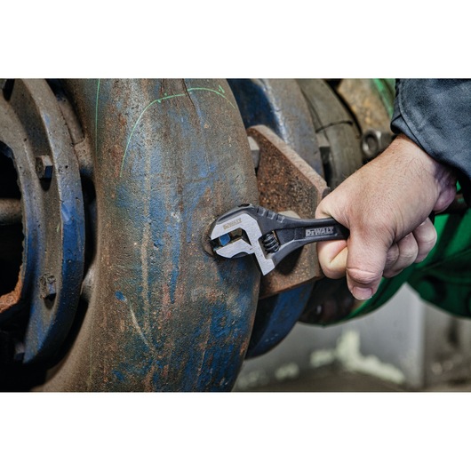 A hand using a DEWALT adjustable wrench to tighten or loosen a bolt on a large, rusted metal pipe.