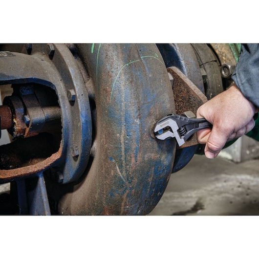 A close-up of a person's hand using a DEWALT adjustable wrench to tighten or loosen a bolt on a large piece of industrial equipment with a rusted surface.
