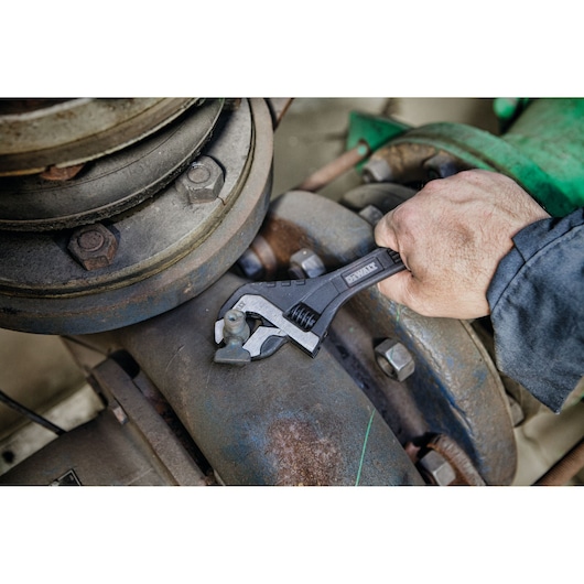 A hand using a DEWALT adjustable wrench to tighten a bolt on industrial machinery.