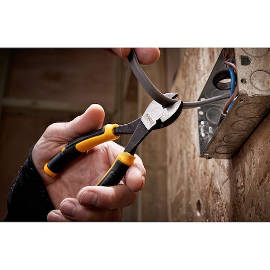 Hand using DEWALT side cutters to trim electrical wire at a wall-mounted metal junction box.
