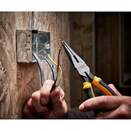 DEWALT pliers used to bend electrical wire near a metal outlet box mounted on a wooden wall.