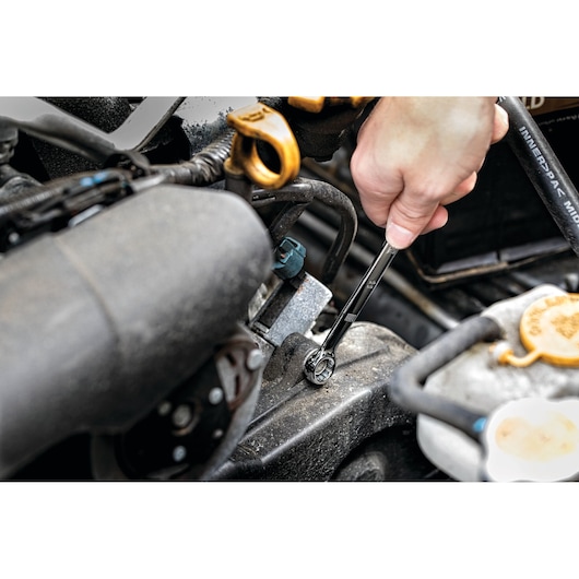 A close-up of a hand using a DEWALT ratcheting wrench to tighten or loosen a bolt on a car engine.