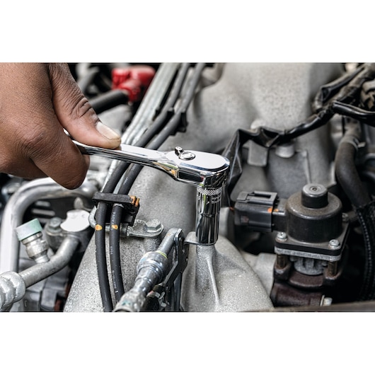 A close-up view of a hand using a DEWALT ratchet wrench to tighten or loosen a bolt on an engine component.