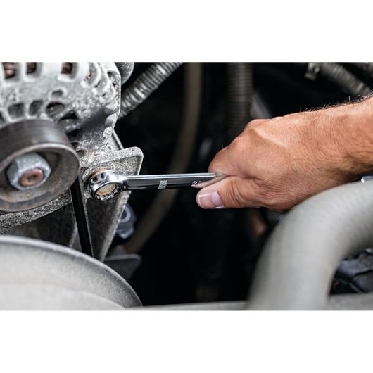 A close-up of a hand using a DEWALT ratcheting combination wrench to tighten a bolt on a piece of machinery.