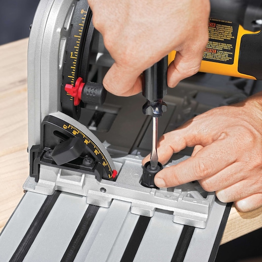 Close-up of hands adjusting a DEWALT track saw using a screwdriver, with visible angle measurements and guide rail on a wooden surface.