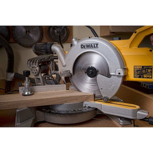 DEWALT DWS778 miter saw cutting wood in a workshop. Saw blade in motion, yellow and silver tool.