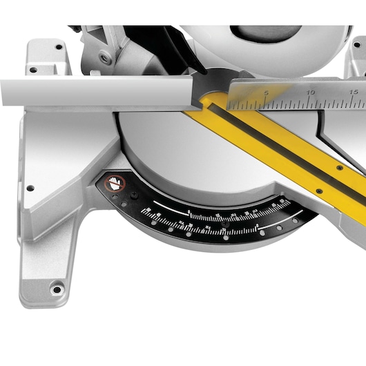 Close-up view of a DEWALT miter saw, model DWS778, showing the miter scale, a measuring ruler, and a piece of material being positioned for cutting.