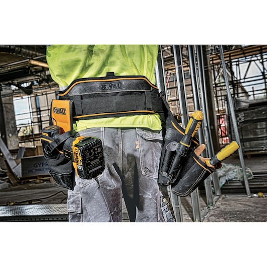 Worker wearing DEWALT tool belt with various tools at a construction site.