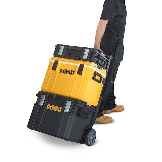 Person pulling a stack of DEWALT toolboxes on wheels, wearing work clothes and boots.