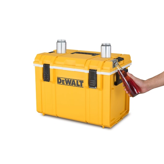 Yellow DEWALT cooler box with bottle opener, two cans on top, and a hand opening a bottle.