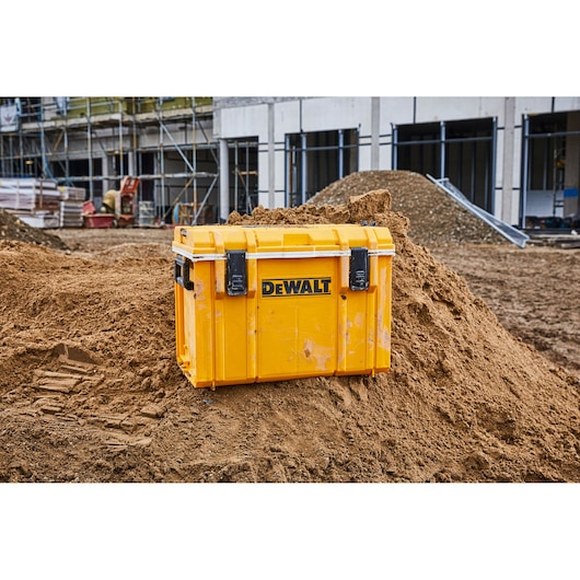 Yellow DEWALT tool box on a dirt mound at a construction site with building scaffolding in the background.