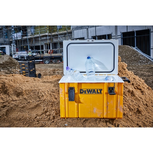 DEWALT yellow cooler box with water bottles on a construction site, lid open and placed on dirt.
