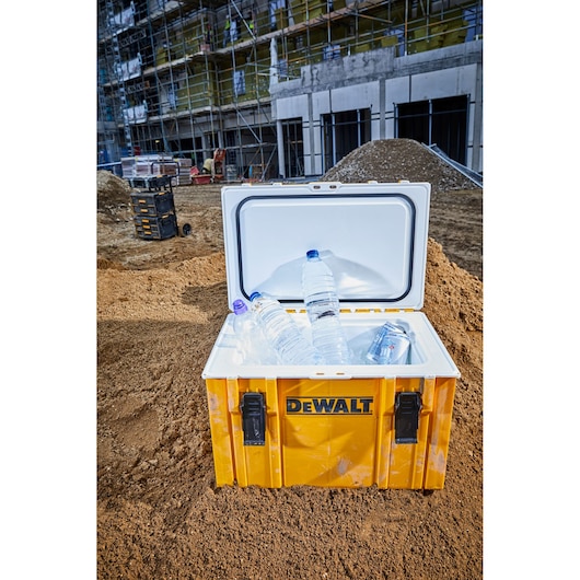 Yellow DEWALT cooler with water bottles and cans on a construction site, lid open.