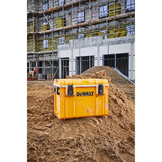 Yellow DEWALT tool storage box on a dirt mound at a construction site with scaffolding in the background.