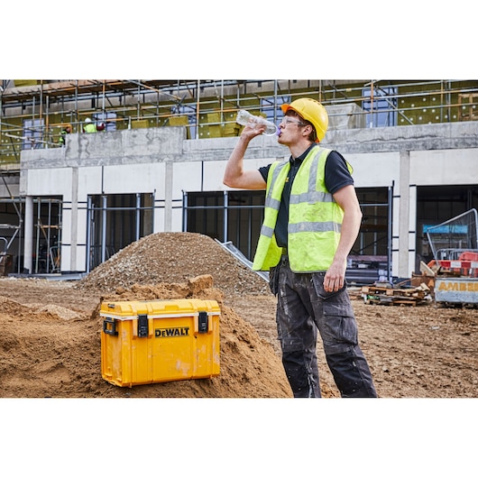 DEWALT storage box on a construction site with a worker in safety gear drinking water nearby.