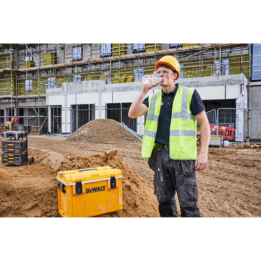 DEWALT storage box on a construction site, worker in safety vest and helmet drinks water.