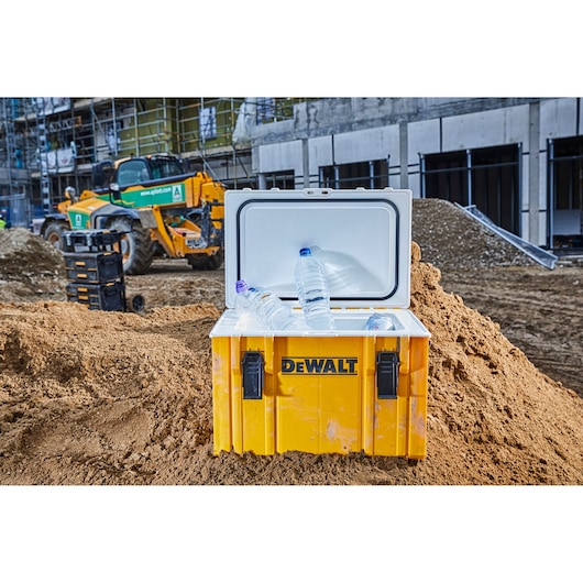 DEWALT cooler box with water bottles, open on a construction site, yellow machinery and buildings in the background.