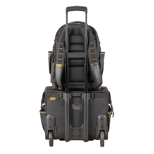 Black DEWALT backpack mounted on a rolling suitcase, shown from the rear with handle extended.