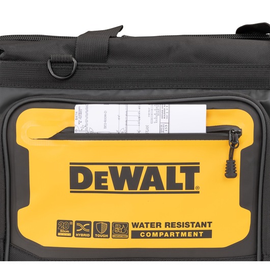 Close-up of a DEWALT black and yellow bag featuring a front compartment with a zipper, containing a rolled technical document. The compartment is labeled 'WATER RESISTANT COMPARTMENT' along with icons for size, hybrid use, toughness, and IP54 rating.