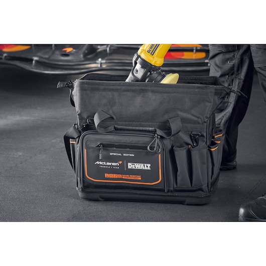 DEWALT McLaren tool bag with multiple compartments, black with orange accents, shown in a workshop setting.