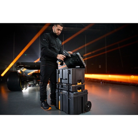 Person using a DEWALT tool storage stack with wheels in an industrial setting, near an illuminated sports car.