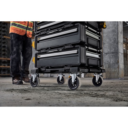 Stacked DEWALT toolboxes on wheels in a construction area, shown near a worker's legs.