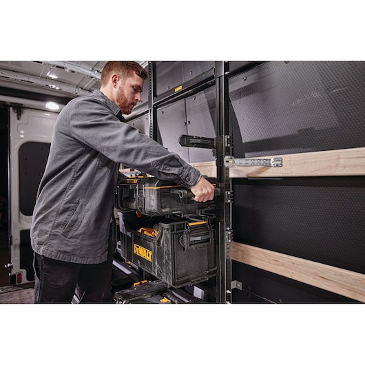 A person is organizing DEWALT tool storage boxes on a shelving unit inside a vehicle. The tool boxes are black with yellow