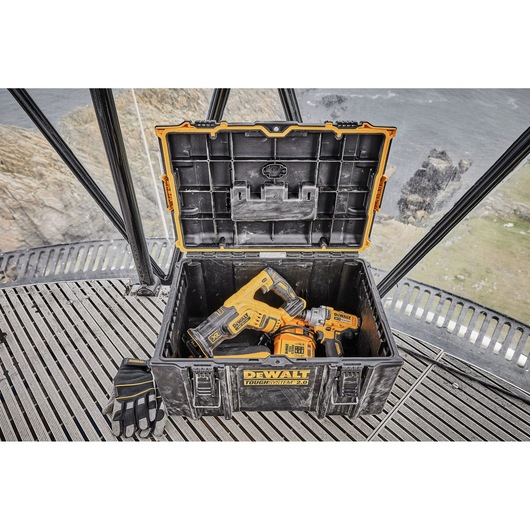 A DEWALT ToughSystem 2.0 tool box with its lid open, containing two cordless DEWALT power tools and a pair of gloves placed